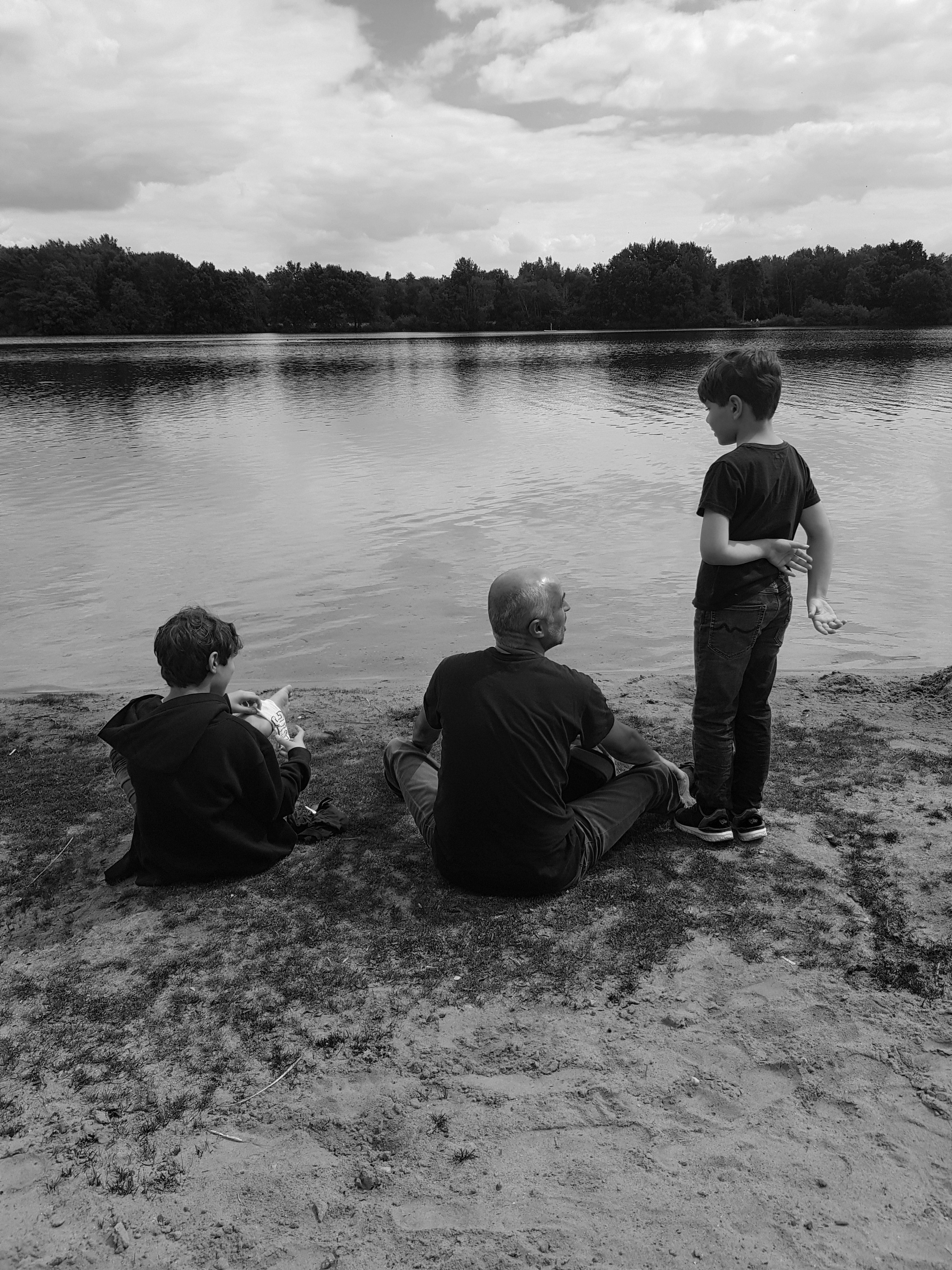Ein Vater und seine zwei Söhne befinden sich am Rand eines Gewässers.